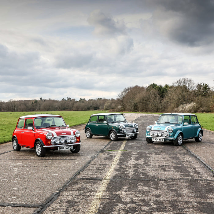 Three Classic Mini Coopers lined up on a racetrack. One red, one dark green, one blue.